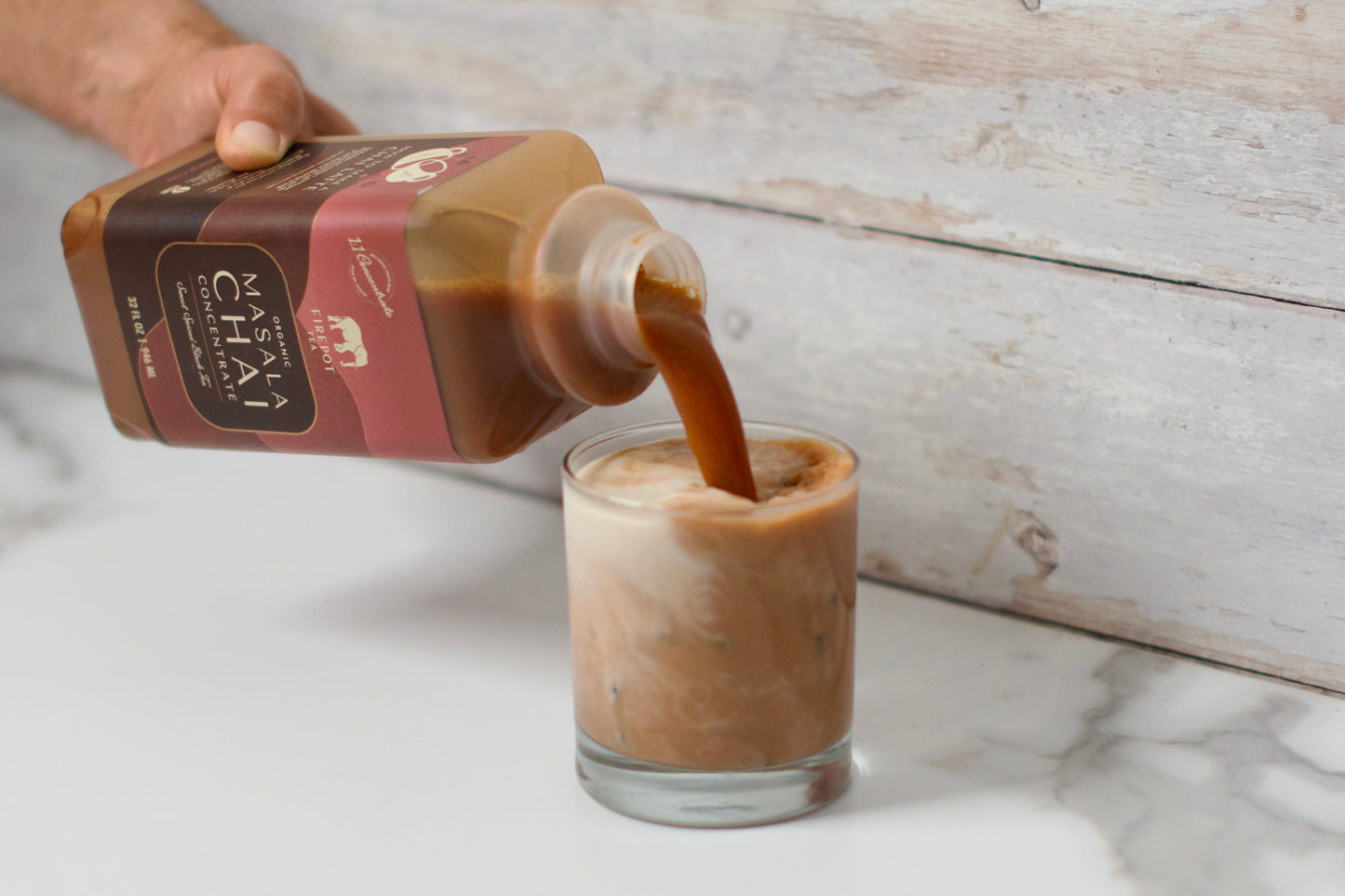 person pouring chai concentrate into a glass with milk